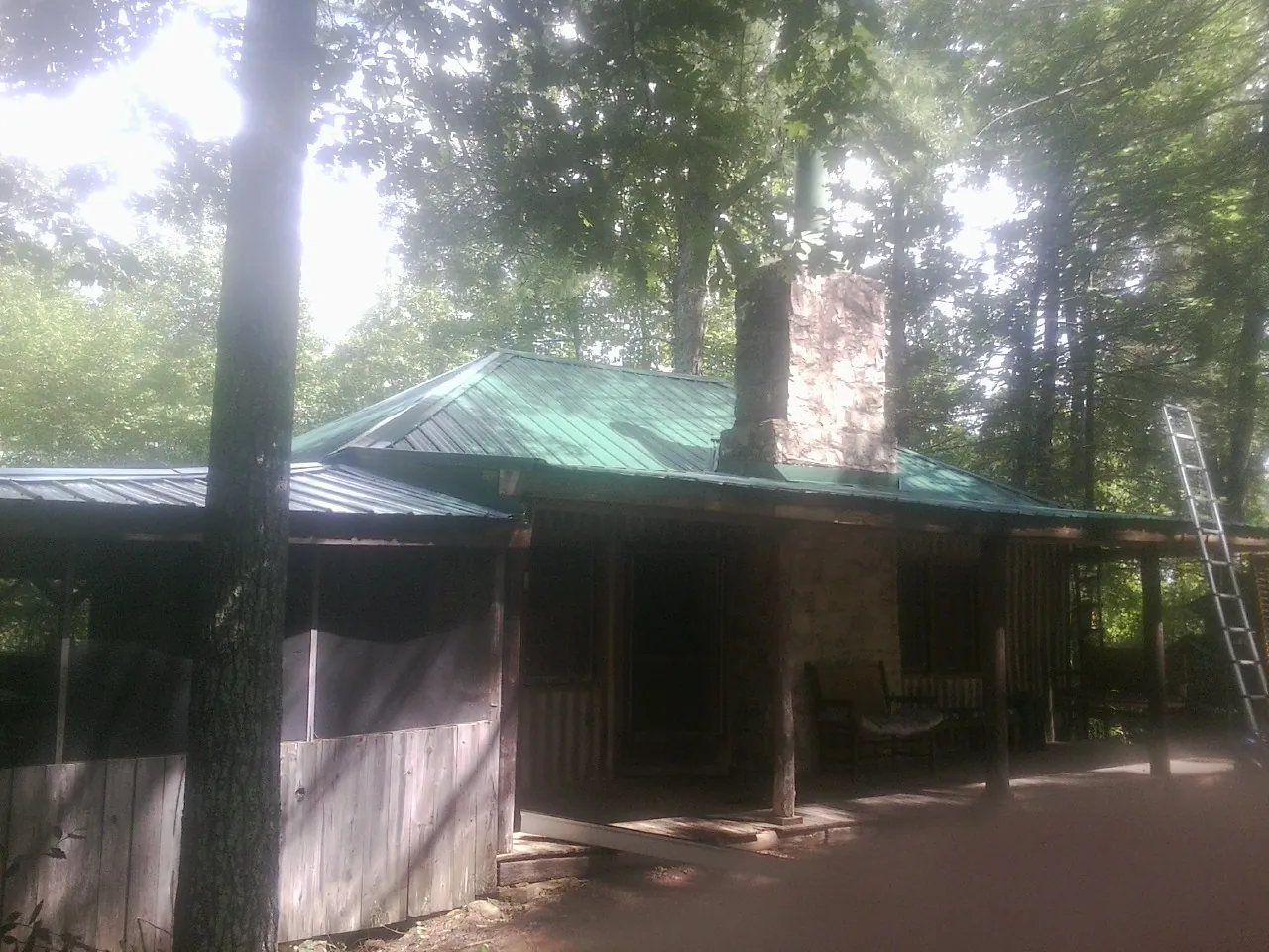 Green metal roof and stone chimney above a log cabin porch in Dyer